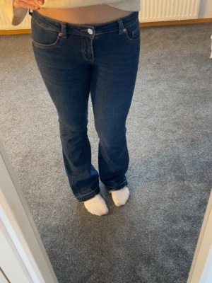 Mörkblå bootcut jeans - Säljer ett par mörkblå uppsprättade bootcut jeans med klassisk femficksdesign och låg midja. Jeansen har en snygg passform som sitter tajt över låren och släpper ut vid bensluten. Tillverkade i stretchigt denimtyg för extra komfort.