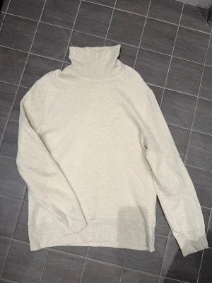 Our Legacy - Mock Neck - Snow Melange - Säljer en stilren snow Melange polotröja med lång ärm. Tröjan har en hög krage och är gjord i ett mjukt material. Perfekt för lager på lager och passar till det mesta. Storlek 52.