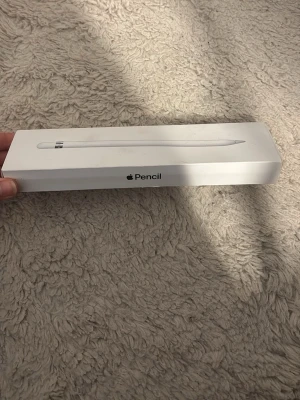 Apple Pencil första generationen - Apple Pencil första generationen i vit färg, levereras i originalförpackning. Pennan är tillverkad i plast och har en stilren, rund design med silverdetalj vid toppen. Perfekt för iPad-användare som vill rita eller anteckna digitalt.