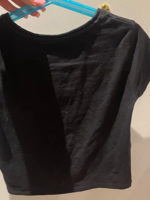 Svart croppad topp från 157 - En enkel och stilren svart croppad topp från 157. Tillverkad i mjuk bomull med lite stretch tack vare elastan. Toppen har korta ärmar och en klassisk rund halsringning. Perfekt att matcha med höga jeans eller kjol.