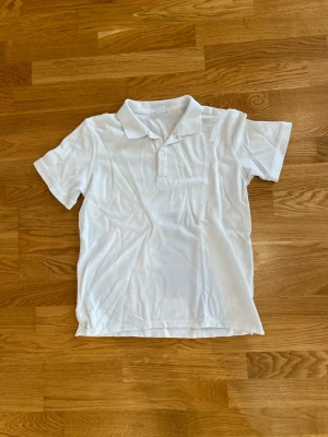 Vit piké t-shirt i bomull - Klassisk vit piké t-shirt med krage och knappar framtill. Tillverkad i mjuk bomull och har korta ärmar. Enkel och stilren design som passar till det mesta. Väldigt skön och stilig! Skriv om du har någon fundering så löser vi det!