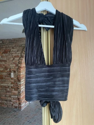 Svart omlott/halterneck topp med knyt - Säljer en svart omlott/halterneck topp med djup ringning och bred knytning i ryggen. Perfekt för fest! Storlek L men på grund av dess justeringar funkar det även på en M eller S 🌻