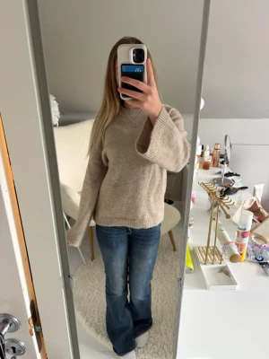 Beige stickad tröja med vida ärmar - Mysig beige stickad tröja med rund hals och vida ärmar. Tröjan har ribbstickade muddar vid ärmslut och nederkant. Inte använd.
