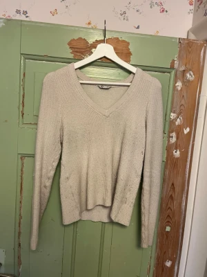 Beige stickad tröja med v-ringning - Mysig beige stickad tröja med v-ringad hals och långa ärmar. Tröjan har ribbad struktur och en något figurnära passform. Storlek M. Från Cubus. Använd och därav nopprig. Hör av er om fler bilder, priset kan alltid diskuteras!