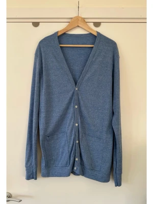 Blå American Apparel kofta, storlek L - Otroligt fin blå / ljusblå melerad kofta från American Apparel i storlek L. Deras mest klassiska modell med långa ärmar och knappar och fickor framtill. Mycket fint skick.   Skickas mot porto, kan även hämtas i Stockholm. 