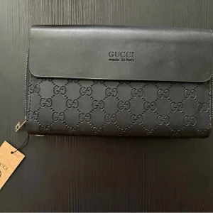 Stor Clutch  - Stor Clutch med sling till, så man kan bära den runt handleden. Finns även så man kan hålla på baksidan. Fack för kort, sedlar och mynt. Ytterligare ett fack för fler kort, sedlar mm. Stängs genom magnet. Helt ny med lapp på. Ungefär 22cm lång och 14cm hög