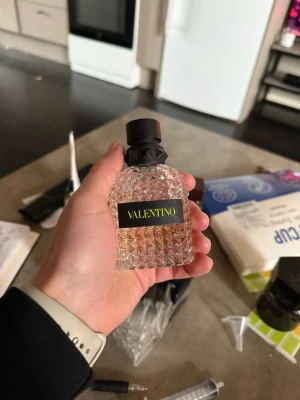 Valentino Yellow Dream - Säljer en lyxig parfym från Valentino i en genomskinlig glasflaska med nitar och svart kork. Flaskan har en elegant design med gulddetaljer och etikett med Valentino-loggan. Perfekt för dig som gillar exklusiva dofter och snygg inredning på sminkbordet. Cirka 40 ml kvar av flaskan 