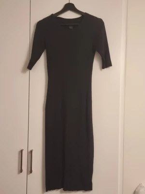 Svart ribbad långklänning Lindex - Svart ribbad långklänning från Lindex i storlek M. Klänningen har en kroppsnära passform, rund halsringning och halvlånga ärmar. Perfekt för dig som gillar en enkel men stilren look.