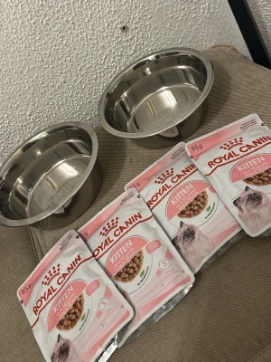 Kattmatskålar och Royal Canin kattmat - Två rostfria matskålar och fyra påsar Royal Canin Kitten våtfoder. Skålarna är silverfärgade och runda, perfekta för kattmat eller vatten. Våtfodret är anpassat för kattungar och kommer i praktiska portionspåsar om 85g.
