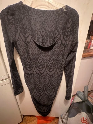 Style ALMA-LS-TURN-DPESS Colour: DARK GREY LALA Style no.:9583 STL M/L  - Klänning med långa ärmar och ett mönster i mörkgrått och svart. Klänningen har en rundad halsringning och är designad med en figurnära passform som framhäver silhuetten. Den har en draperad effekt längs sidorna, vilket ger en smickrande form. Klänningen är lämplig för olika tillfällen, från vardagsbruk till mer uppklädda evenemang. Jag fick den i en mysteriebox från MollyandMy men är inte min still. Det är helt oanvänd inte ens provad. Är cirka 132 cm lång.  