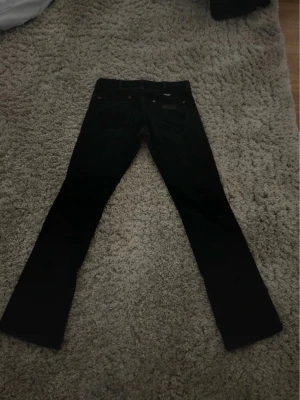 Svarta bootcut jeans - Säljer ett par supersnygga svarta Wrangler jeans! Dom är lågmidjade med bootcut och har superfina detaljer på fickorna och på knappen! Storleken är W27 L32 men skulle säga att det är någorlunda mindre, skriv för mått!