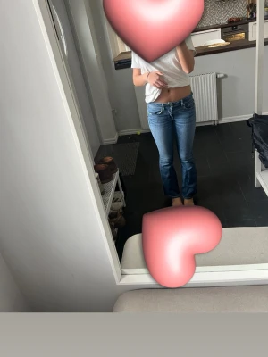 Blå bootcut jeans med låg midja - Säljer ett par blå bootcut jeans med låg midja och klassiska fem fickor. Jeansen har en snygg tvätt och sitter tajt över låren för att sedan bli vidare nedtill. Perfekta för en trendig och avslappnad stil.