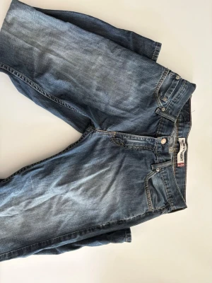 Retro Levi's 514 jeans - Retro blå Levi's 514 jeans med raka ben och femficksmodell. Jeansen har en ljus tvätt, knappgylf och ikoniska bakfickor med broderad båge samt läderpatch i midjan. Perfekta för en avslappnad och tidlös stil.