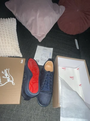 Marinblå sneakers från Louboutin - Snygga marinblå sneakers från Christian Louboutin med klassisk röd sula och diskret logga på sidan. Skorna har en låg profil, rund tå och är tillverkade i mocka med matchande skosnören. Perfekta för dig som vill sticka ut med exklusiv streetstyle.