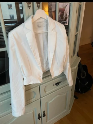 Vit croppad kavaj från NLY Trend - Snygg vit croppad kavaj från NLY Trend med klassisk krage och knapp framtill. Kavajen har lång ärm och en stilren, minimalistisk look som passar till många olika outfits. 