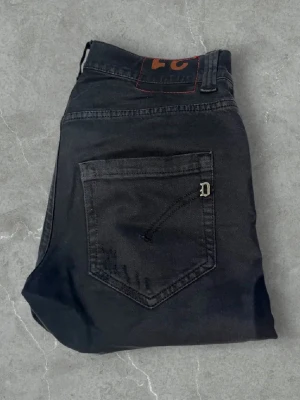 Svarta jeans från Dondup - Säljer ett par svarta jeans från Diesel med slitna detaljer och en klassisk femficksmodell. Jeansen har en rak passform och en liten metallogo på bakfickan. Perfekta för en edgy och avslappnad stil. Modell: George 