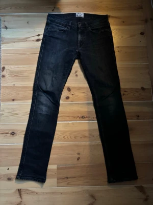 Marinblåa raka jeans från Acne Studios - Säljer ett par svarta jeans från Acne Studios med rak passform och klassisk femficksdesign. Jeansen har subtila slitningar och är tillverkade i ett mjukt denimtyg som ger en snygg och avslappnad look. Perfekta för dig som gillar stilrena och tidlösa plagg.