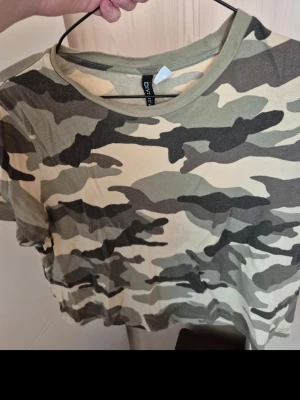 Camouflage t-shirt magtröja - Säljer en kortärmad t-shirt från Divided med klassiskt camouflage-mönster. Det är en magtröja.