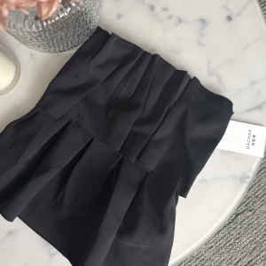 Svart bandeau topp från Dagmar - Säljer en svart bandeau topp från Dagmar med snygga veckade detaljer framtill. Aldrig använd då den var för liten. Prislapp kvar. Nypris 3000kr