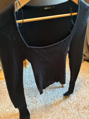 Svart stickad tröja Gina Tricot - Snygg svart stickad tröja från Gina Tricot med bred, djup urringning och långa ärmar. Tröjan har en smal passform och är tillverkad i mjukt, ribbat material som ger en stilren look. Perfekt att matcha med jeans eller kjol.