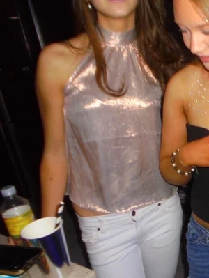 Rosa halterneck topp - Säljer en glittrig rosa halterneck topp med hög hals och ärmlös design. Toppen har en lös passform och ett skimrande material som fångar ljuset snyggt. Perfekt för dig som vill sticka ut lite extra.