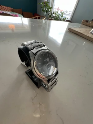 Klassisk silverfärgad inex klocka - Stilren klocka från inex med svart urtavla och datumvisning. Armbandet är i metall med klassisk länkdesign och boetten är rund i silverfärg. Perfekt accessoar för dig som gillar en tidlös look.