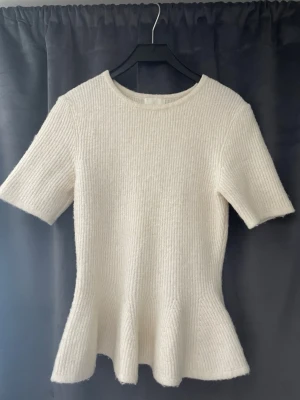 Beige stickad blus från H&M - Säljer en jättefin beige stickad blus från H&M med korta ärmar och rund halsringning. Blusen har en lätt utsvängd midja som ger en snygg siluett och är stickad i ett mjukt material. Perfekt för dig som gillar enkel men stilren design. Pris kan diskuteras💕