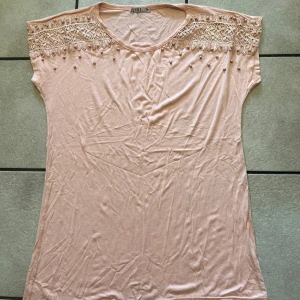 Ljusrosa topp med spets och pärlor - Supersöt ljusrosa topp från ESLI Fashion med bred spets upptill och dekorativa pärlor längs axlarna. Toppens material är mjukt och lätt, perfekt för varmare dagar. Den har rund halsringning och är ärmlös med en feminin och romantisk vibe.
