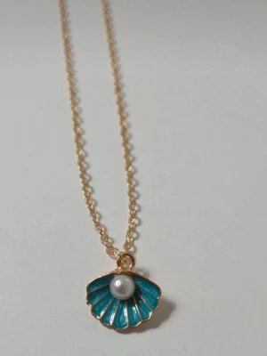 Halsband med blå snäcka och pärla - Snyggt halsband med tunn guldfärgad kedja och ett hängsmycke i form av en blå snäcka med en vit pärla i mitten. Perfekt accessoar för dig som gillar havsinspirerade detaljer. Kedjan är enkel och smidig, och snäckan har fina guldfärgade kanter.