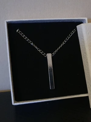 STAINLESS STEAL - HALSBAND - Ett stilrent halsband i rostfritt stål med ett elegant, rektangulärt hänge. Den minimalistiska designen förmedlar både styrka och finess, vilket gör det till ett självklart val för vem som helst.