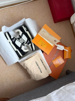 Louis Vuitton svartvita sneakers - Snygga svartvita Louis Vuitton sneakers med klassisk LV-logga på plösen och sidan. Skorna har vita snören, svarta detaljer och en robust sula. Tillverkade i läder och textil med exklusiva detaljer och mönster. Kommer med originalkartong och dustbag.