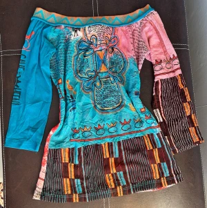 Så fin offshoulder tröja från Save the Queen! - Unik offshoulder tröja från Save the Queen med färgstarkt mönster i blått, rosa, rött och brunt. Tröjan har trekvartsärm, asymmetriskt mönster med kronor, ränder och grafiska detaljer. Otroligt fynd 👑