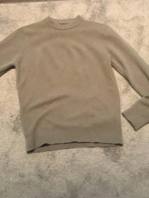 Grön stickad tröja  - En enkel och stilren beige stickad tröja med rund halsringning och långa ärmar. Tröjan har ribbstickade muddar vid hals, ärmslut och nederkant. Perfekt för lager på lager och passar till det mesta.