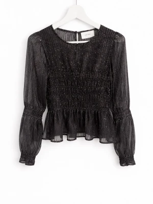 Svart glittrig blus från Neo Noir - Supersnygg svart blus från Neo Noir med glittriga trådar, smockad midja och volangkant nedtill. Blusen har transparenta långärmar och rund halsringning. Perfekt för att lyfta vilken outfit som helst!