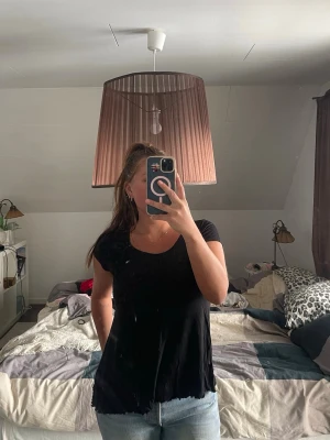 Svart topp med blomdetalj från Kappahl - Svart topp från Kappahl med kort ärm och rund halsringning. Toppen har en dekorativ svart blomma på axeln och lätt utställd passform. 