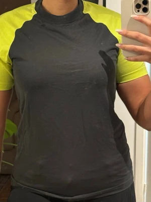 Svart och gul t-shirt med kontrastärmar - Cool t-shirt i svart med neongula kontrastärmar och axelparti. Klassisk rund halsringning och jobb vibe, perfekt för dig som vill ha en jobb topp. Materialet känns som bomull eller polyester, stretchigt och bekvämt. Finns 2 av varje 120 för 4st