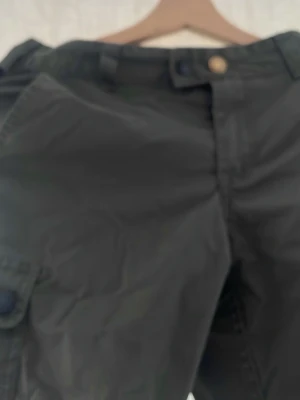 Gröna cargobyxor med svarta detaljer - Säljer ett par gröna cargobyxor med svarta förstärkningar på knän och benslut. Byxorna har flera fickor, bland annat en klassisk cargoficka på sidan. Perfekta för dig som gillar en funktionell och cool stil.