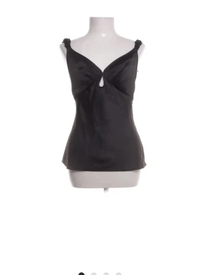 Elegant svart satin-topp med unika detaljer  - Säljer en otroligt fin och stilren svart topp i ett material med vacker lyster. Perfekt för både festliga tillfällen och som ett lyxigt basplagg under en kavaj.   