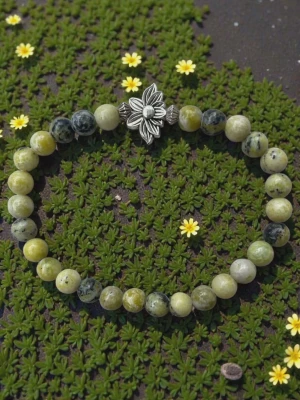 Grönt pärlarmband med blomdetalj - Snyggt armband med runda pärlor i olika nyanser av grönt och grått. Armbandet har en dekorativ silverfärgad blomma i metall som detalj. Perfekt accessoar för dig som gillar naturinspirerad stil och unika smycken.