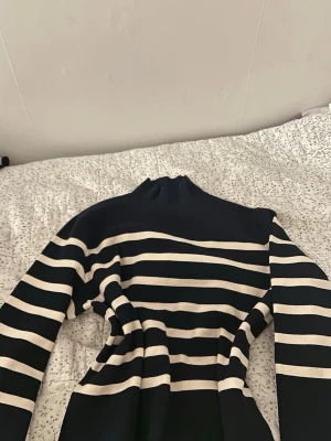 Svartvit randig stickad tröja - Säljer en svart stickad tröja med breda vita horisontella ränder. Tröjan har hög hals och långa ärmar, samt ribbade kanter vid ärmslut och nederkant. Perfekt för dig som gillar klassisk och stilren design. Diskuterar pris ect🌸