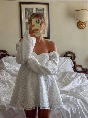 Vit klänning - Superfin vit kortklänning med offshoulder och långa puffärmar. Klänningen har vackra spetsdetaljer med blommigt mönster och en lätt utsvängd kjol. Perfekt för sommarens alla tillfällen och till studenten!