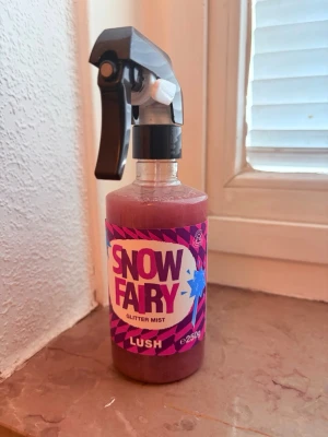 Lush Snow Fairy Glitter Mist 250g - Snow Fairy Glitter Mist från Lush är en rosa parfymmist med glittereffekt. Flaskan har en sprayfunktion och rymmer 250g. Doften är söt och fruktig med inslag av citrus och persika. Perfekt för dig som vill ha en glittrande finish och en unik doft.