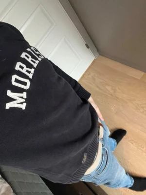 Mörkblå stickad tröja från Morris - Säljer en mörkblå stickad tröja från Morris med vit text framtill. Tröjan har rund halsringning, ribbade muddar och är långärmad. Perfekt för dig som gillar klassisk och stilren design.