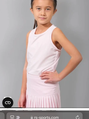 Ljusrosa sportlinne rs tennis - Snyggt ljusrosa sportset med ärmlöst. Perfekt för tennis eller andra sportaktiviteter. Linnet har rund halsringning. Materialet ser ut att vara lätt och andas.