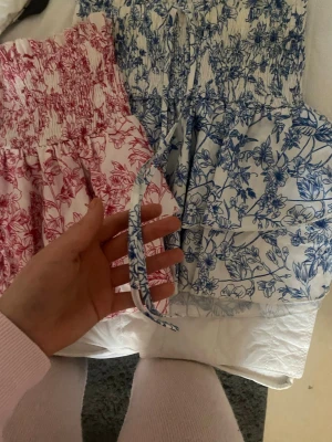 Blommig kortklänning med snörning - Supersöta kjolar med volangig kant. Finns i både ljusrosa o ljusblå. Kjolen har smala snören ”detaljer” längst upp och är perfekt för varma dagar. Materialet känns lätt och luftigt. Storlek xs/s men passar upp till M dem kan stretchas ut väldigt långt. Köp båda för 150 eller än för 90.