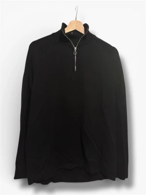 Svart halvzip tröja med hög krage - Stilren svart tröja med halv dragkedja och hög krage. Långärmad modell i mjukt material som passar perfekt till lager-på-lager. Enkel och clean design utan synliga loggor eller mönster.