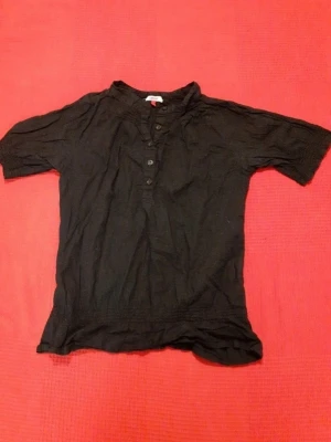 Svart kortärmad blus från ONLY - Svart blus från ONLY med korta ärmar och knappar framtill. Blusen har en enkel och avslappnad design med mjukt tyg och lätt struktur. Perfekt för dig som gillar stilrena plagg med en klassisk touch.