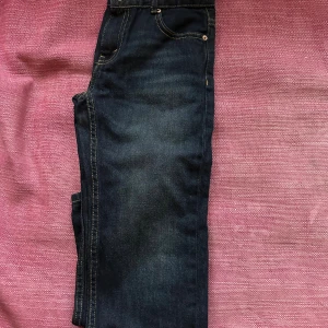 Mörkblå jeans med kontrastsömmar - Snygga mörkblå jeans med en fin mörkblå färg pch en klassisk femficksdesign och kontrastsömmar. Jeansen har en rak passform och detaljer i brunt läder vid linningen. Perfekta för en avslappnad och trendig look. Skicket är nästan som nytt!