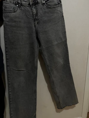 Grå raka jeans med fem fickor - Säljer ett par grå jeans med rak passform och klassisk femficksdesign. Jeansen har en tvättad look och normal midja. Materialet är denim i bomull och de har bälteshällor samt knappgylf. Perfekta för en avslappnad stil.