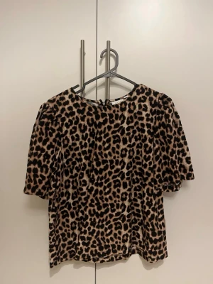 Leopardmönstrad topp med puffärm - Säljer en snygg topp med leopardmönster och puffiga korta ärmar. Toppen har rund halsringning och är i mjukt material som känns skönt mot huden. Har en dragkedja i ryggen. Från VILA.